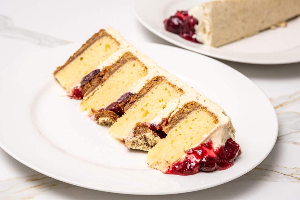 Slice of cherry cheesecake layer cake with graham crumb crust on each layer, cream cheese filling and sour cherry sauce