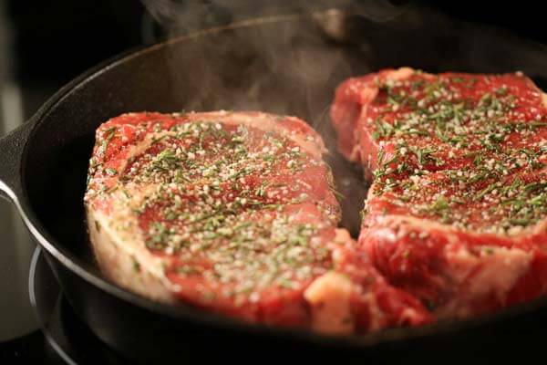 Ribeye steaks searing in a cast-iron pan