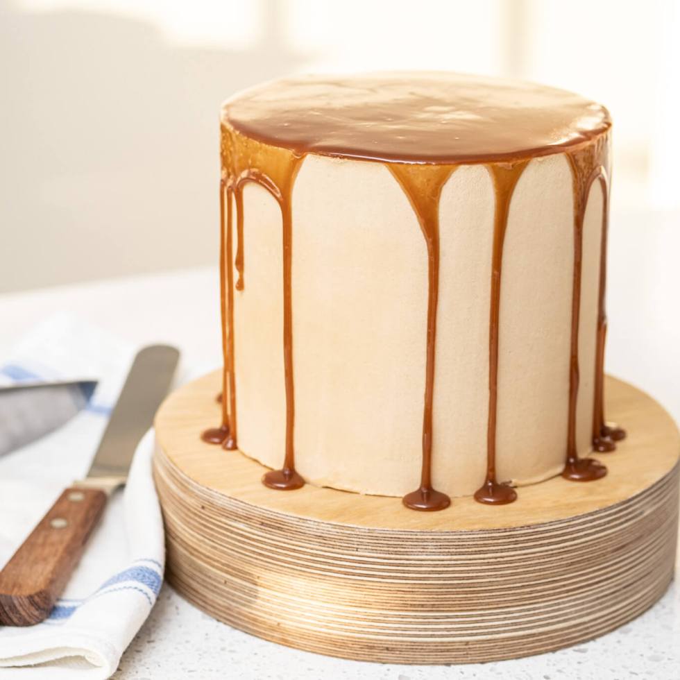 Caramel apple cheesecake cake with caramel drizzle on a wooden cake stand