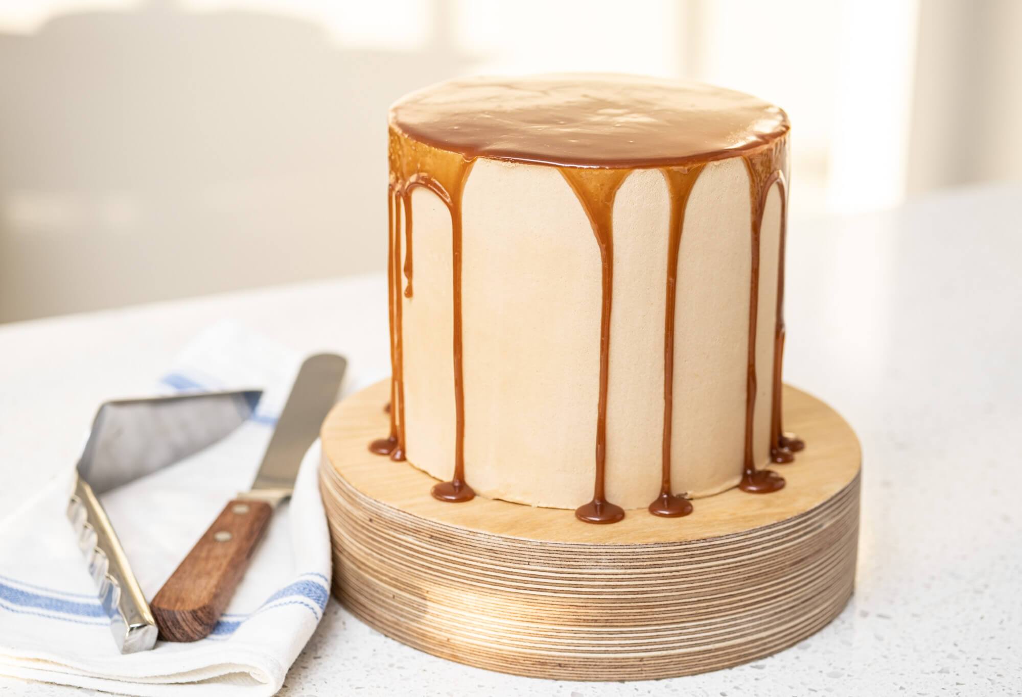 Caramel apple cheesecake cake with caramel drizzle on a wooden cake stand