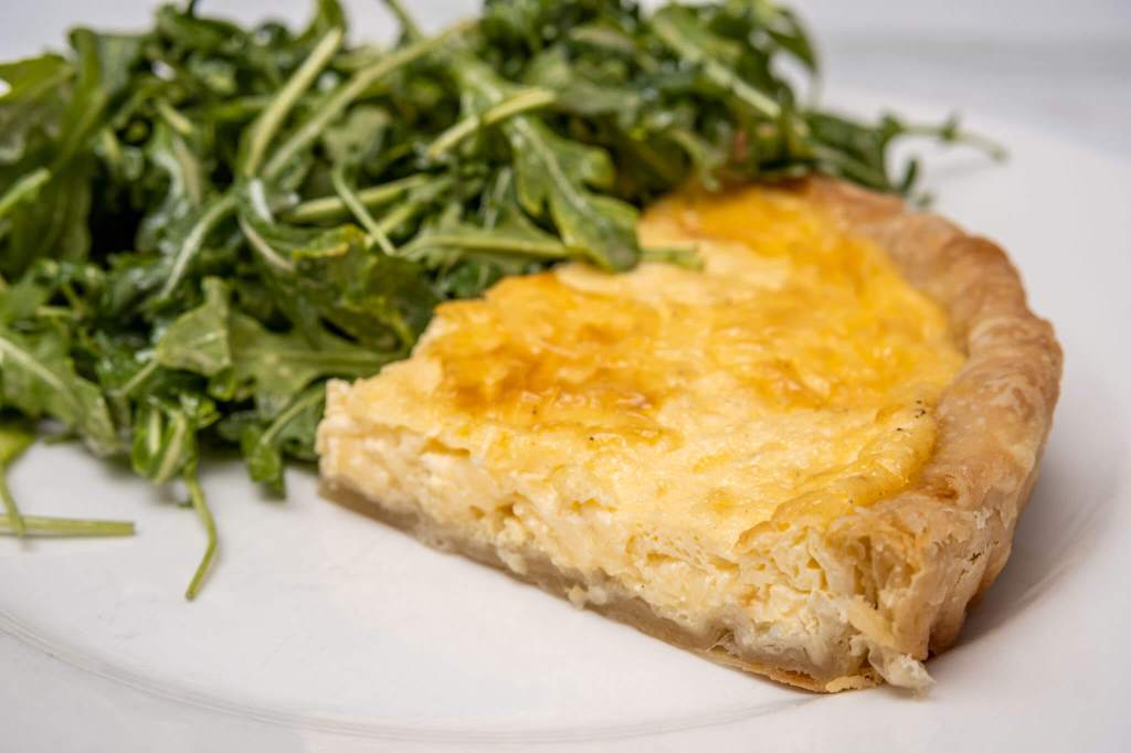 Slice of cheese quiche with an arugula salad