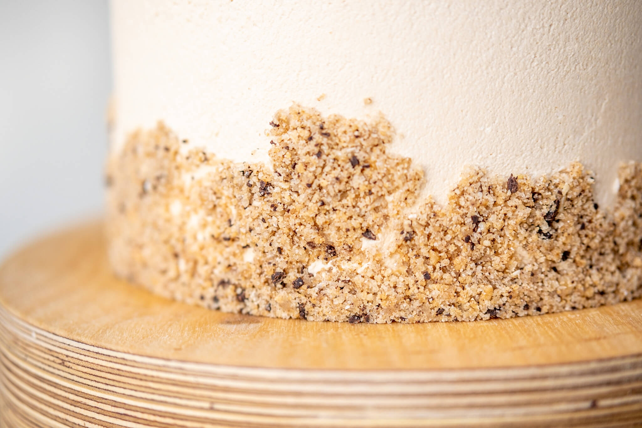 Detail photo of cake crumbs decorating on the bottom of a layer cake, on a plywood cake stand