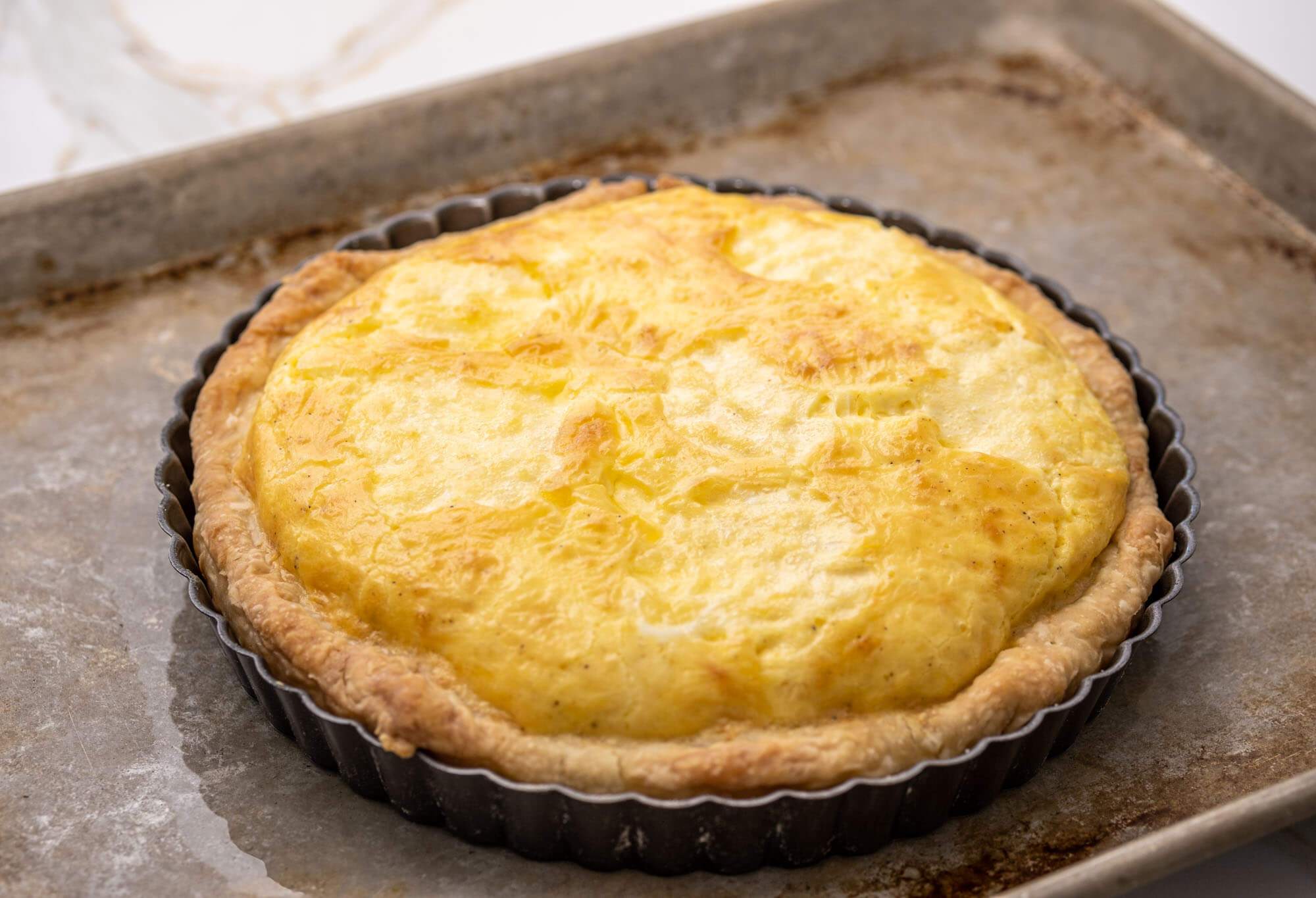 A whole cheese quiche in a tart pan on a baking sheet