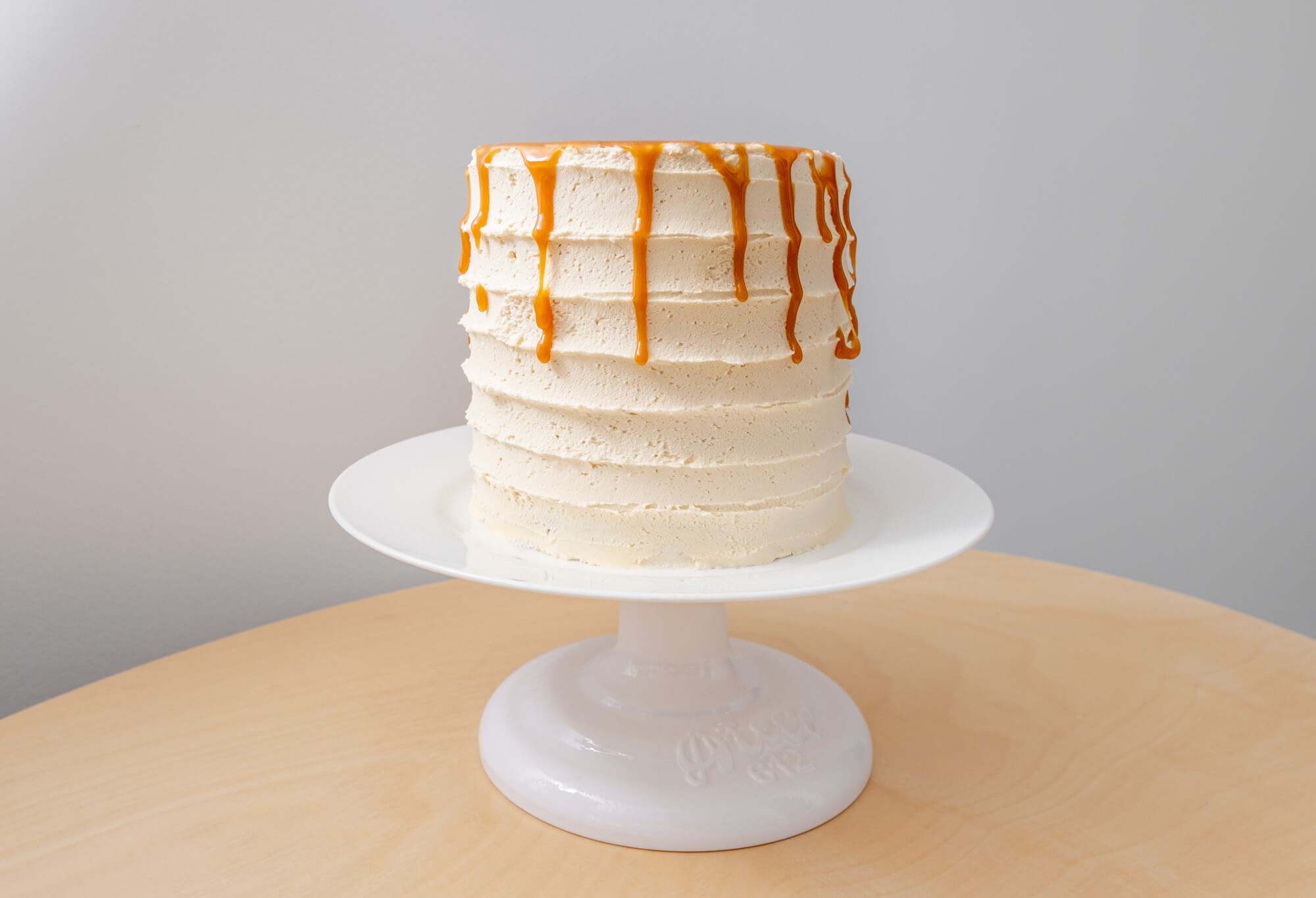 Vegan caramel cake with salted caramel sauce drizzle on a white cake stand