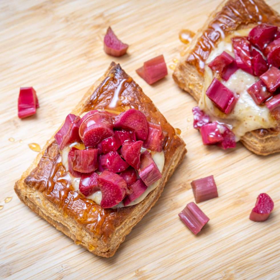 Two puff pastry tarts with almond pastry cream and pieces of poached rhubarb, on a bamboo cutting board